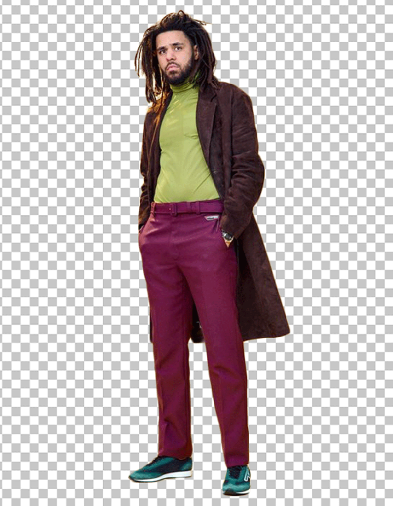 J Cole standing in a green t-shirt, purple pants, and a brown coat.