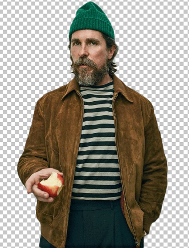 Christian bale is wearing a brown leather jacket and a green beanie, holding an apple in his hand.