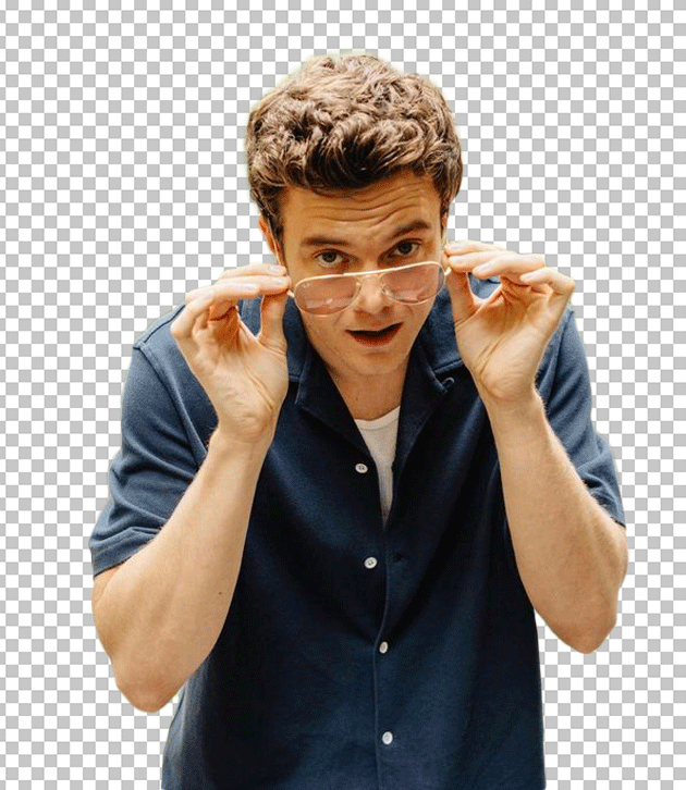 Jack Quaid was staring, wearing a blue shirt, and holding a pair of glasses in front of his face.